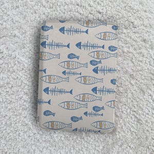 May include: A rectangular, beige item featuring a repeating pattern of blue and orange fish skeletons. The fish skeletons are of different sizes and orientations, creating a whimsical design. The item appears to be a case or cover.