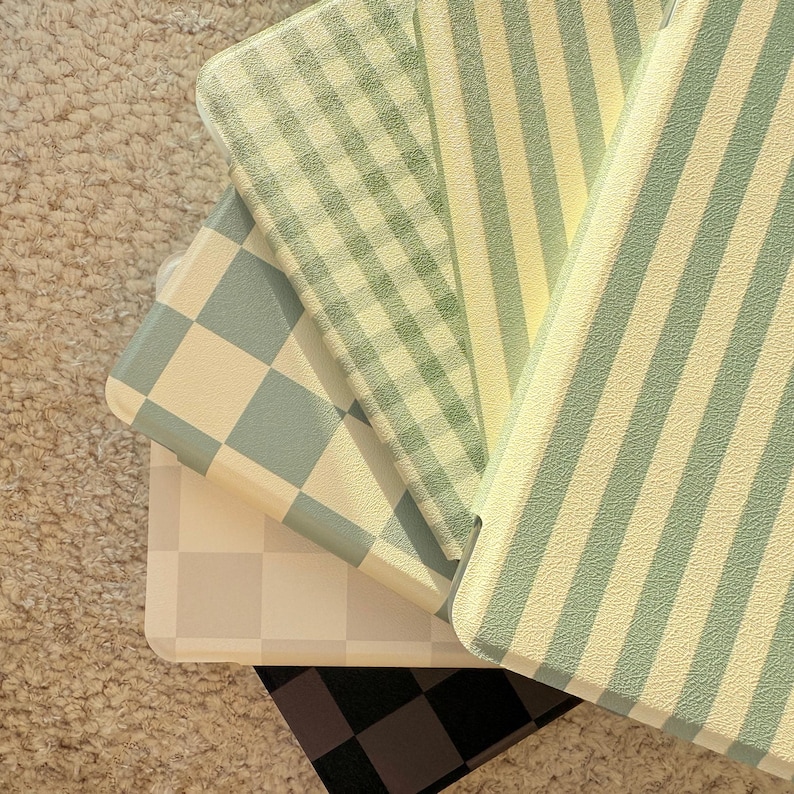 May include: A collection of pastel-colored phone cases with various patterns. The designs include checkered, striped, and gingham patterns in shades of green, blue, and cream. The cases are stacked, showcasing the different designs.