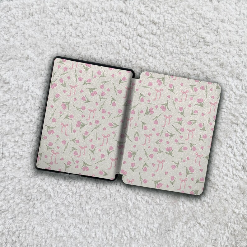 May include: A rectangular e-reader case featuring an all-over pattern of small pink tulips and light pink ribbons on a white background. The case is shown in an open position, displaying the interior panels with the same floral and ribbon design.