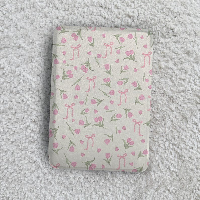 May include: A rectangular object featuring a light beige background with a repeating pattern of small pink tulips with green stems and leaves, interspersed with delicate pink ribbon bows scattered across the entire surface.