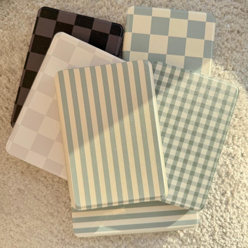 May include: A collection of decorative rectangular coasters with various patterns. Designs include checkered, striped, and gingham patterns in shades of black, white, and blue. The coasters are arranged on a light-colored, textured surface.