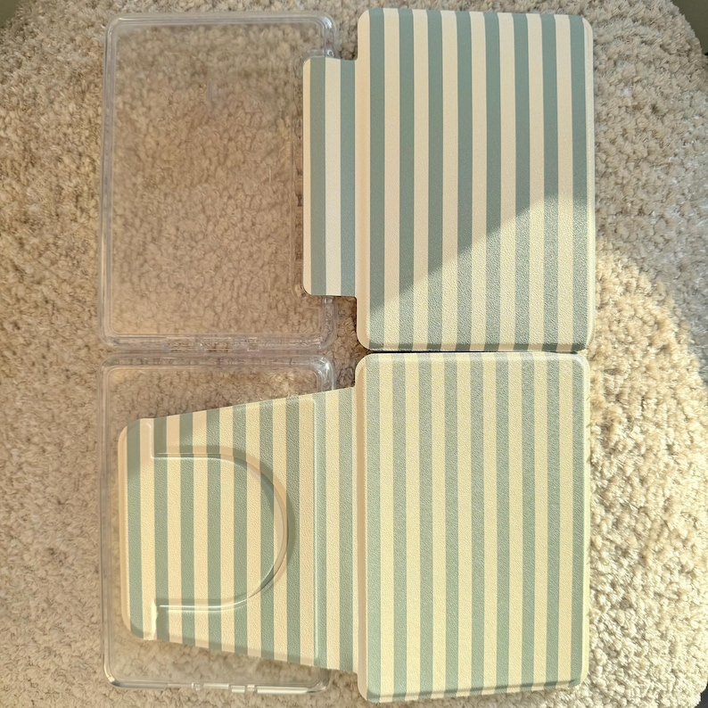 May include: A clear plastic case and a striped case with a light blue and cream vertical stripe pattern. The striped case is open, revealing the interior. The cases are likely for an electronic device.