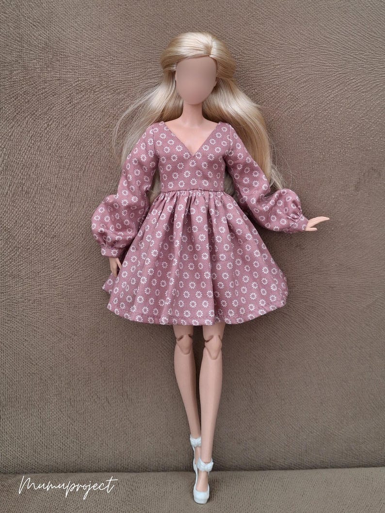 May include: A doll with long blonde hair wearing a dusty rose dress featuring a white daisy pattern, a V-neckline, and long puffed sleeves with cuffs. The doll is wearing white high-heeled shoes. The text "mumuproject" is visible in the bottom corner.