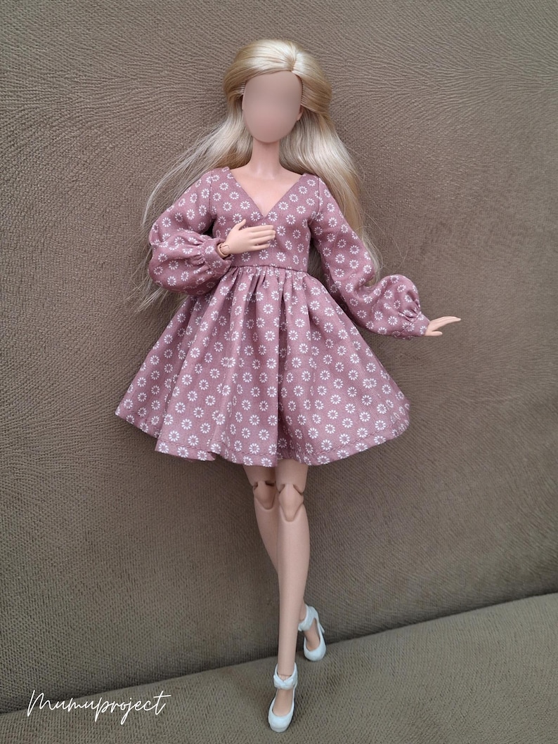 May include: A doll with long blonde hair wearing a mauve dress featuring a white daisy pattern, a V-neckline, and long puffed sleeves with cuffs. The doll has articulated joints and is wearing white shoes. The text mumuproject is visible.