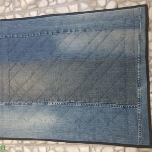 May include: A rectangular denim rug with a quilted diamond pattern in shades of blue and grey. The rug has a black trim and appears to be made from recycled denim.
