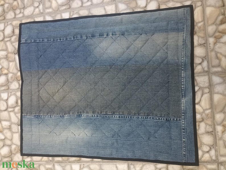 May include: A rectangular denim rug with a quilted diamond pattern in shades of blue and grey. The rug has a black trim and appears to be made from recycled denim.