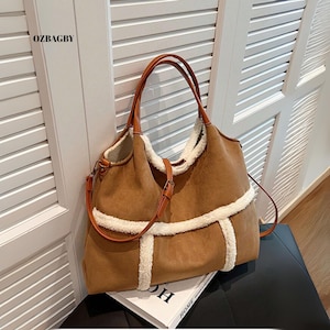 May include: A brown suede tote bag with a cream-coloured faux fur lining and trim. The bag has brown leather handles and a detachable shoulder strap. The brand name "OZBAGBY" is visible on the upper left corner.