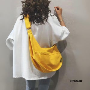 May include: A bright yellow shoulder bag with a single front pocket and adjustable strap. The bag is worn over the shoulder. The text "OZBAGBY" is visible on the lower right corner.