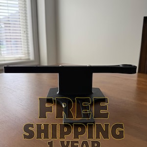 May include: A black metal object with a rectangular base and a horizontal arm. The arm has a circular opening on one end. The object is on a wooden surface. The image also contains the text "FREE SHIPPING 1 YEAR WARRANTY".