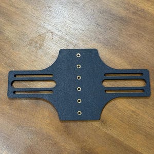May include: A black, rectangular object with a series of small, evenly spaced holes and two horizontal slots on each side. The object appears to be made of a solid, possibly metal, material.