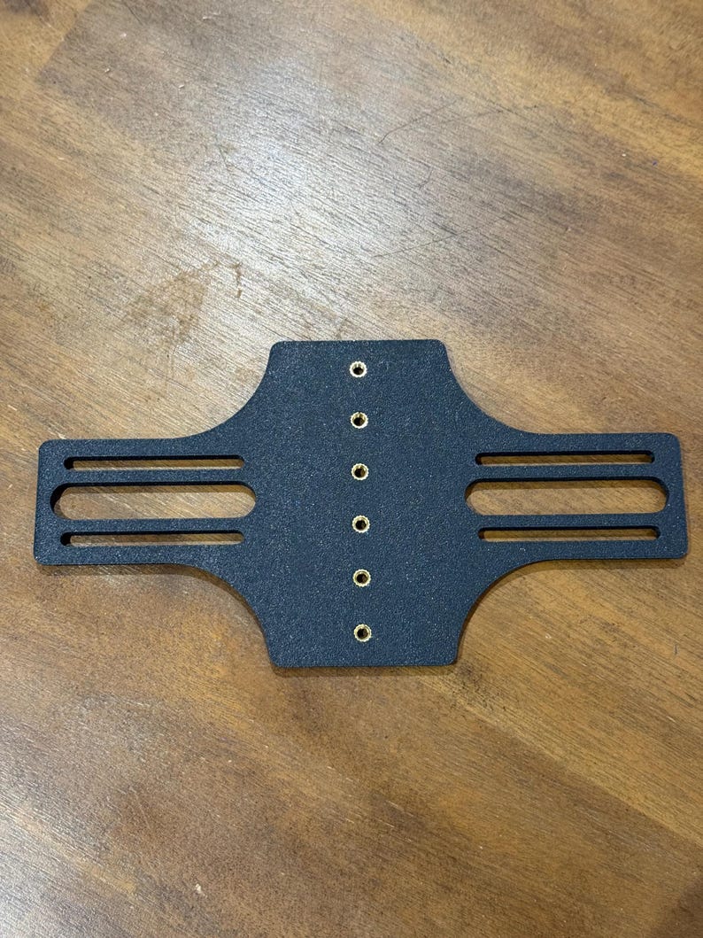 May include: A black, rectangular object with a series of small, evenly spaced holes and two horizontal slots on each side. The object appears to be made of a solid, possibly metal, material.