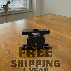 Peut inclure: Un support métallique noir avec plusieurs trous de vis. Le support est posé sur une surface en bois. Le texte "FREE SHIPPING 1 YEAR WARRANTY" est de couleur or.