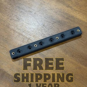May include: A black rectangular object with multiple circular holes and gold-colored accents. The object is positioned diagonally on a wooden surface. The text "FREE SHIPPING 1 YEAR WARRANTY" is visible.