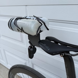 May include: A black bicycle with a black seat and a water bottle holder. The water bottles are clear with black accents. The seat has the text "Selle Italia" on it. The bicycle wheel is visible in the foreground.