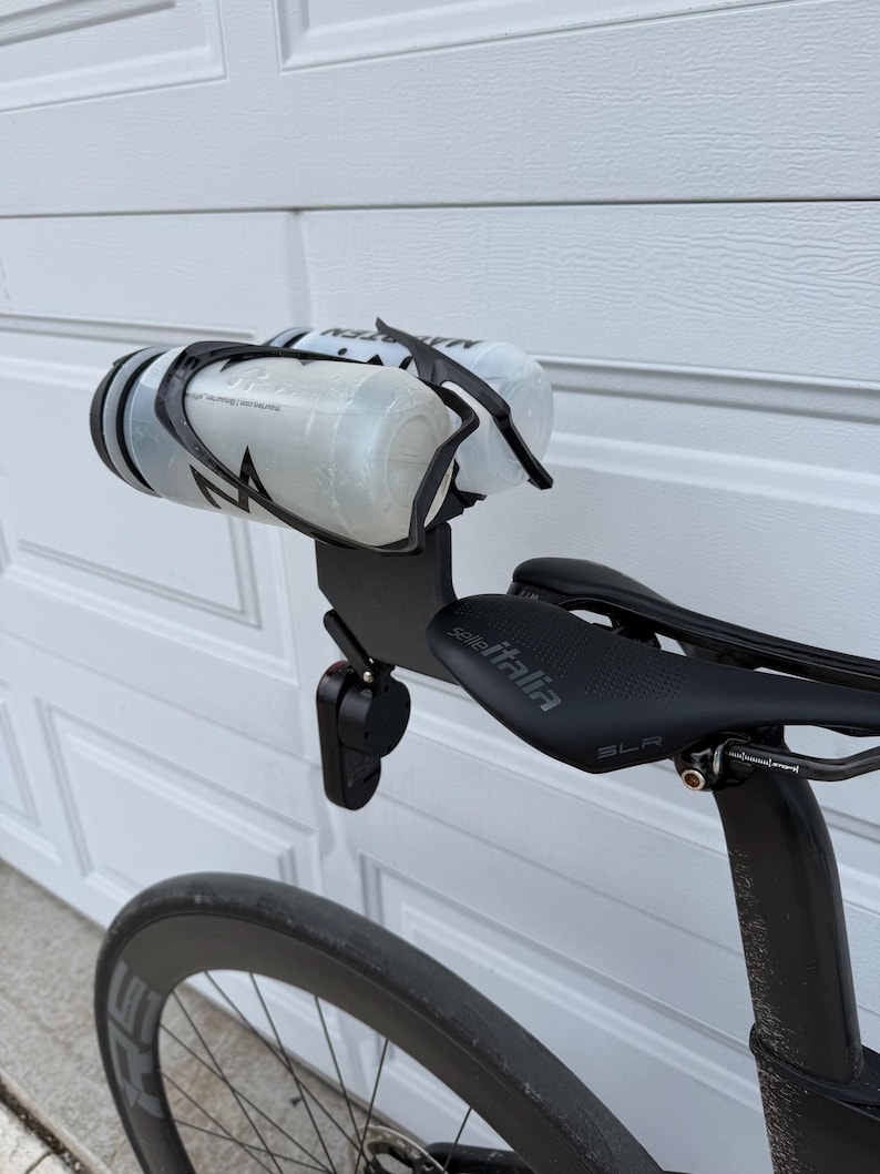 May include: A black bicycle with a black seat and a water bottle holder. The water bottles are clear with black accents. The seat has the text "Selle Italia" on it. The bicycle wheel is visible in the foreground.