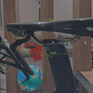 May include: Black bicycle seat with a water bottle cage attached. The seat has a sleek design and is mounted on a black post. Measurements are indicated in cm.