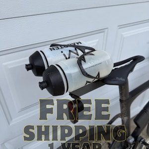 May include: Two water bottles attached to a black bicycle seat. One bottle is white with black text, the other is clear. The bicycle is black. The text "MAGTEN" is visible on the bottles.