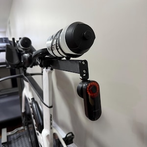 Puede incluir: Una bicicleta de carretera blanca con una extensi&oacute;n de manillar negra que sostiene una botella de agua y una luz trasera roja. La botella de agua es blanca con detalles y texto en negro. La luz trasera es negra con luz roja.