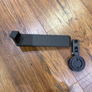 Puede incluir: Soporte negro para ordenador de bicicleta con un brazo rectangular y una base redonda. El soporte est&aacute; hecho de un material negro mate y est&aacute; dise&ntilde;ado para fijarse al manillar de una bicicleta.