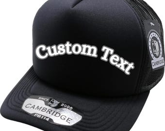 Op de afbeelding: Zwarte truckerpet met de tekst "Custom Text" in witte letters. De pet heeft een mesh achterkant en een gebogen klep. Een label aan de zijkant leest "Cambridge" en "PB114".