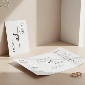 Könnte beinhalten: Eine Hochzeitseinladungssuite mit einer gefalteten Einladung und einer Karte mit den Namen "Olivia and Kevin" in eleganter Schrift. Zwei goldene Eheringe liegen auf dem Tisch. Die Suite befindet sich auf einer hellen Holzoberfläche.