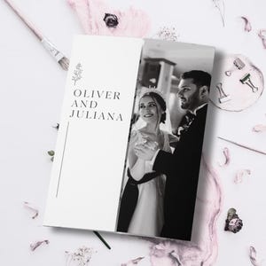 May include: A wedding invitation featuring a black and white photograph of a couple dancing. The left side of the invitation has the names "OLIVER AND JULIANA" in a serif font, with a floral design. The invitation is surrounded by pink floral decorations.