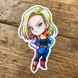 May include: A die-cut sticker featuring a stylized anime character with blonde hair, blue eyes, and a serious expression. The character wears a black top, blue denim skirt, black leggings, brown boots, and an orange neck scarf with a denim jacket.