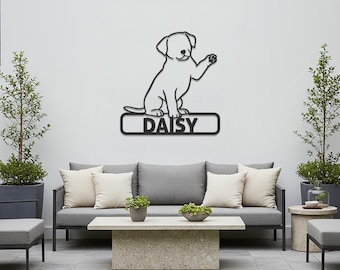 May include: Black metal wall art featuring a stylized puppy waving its paw. The puppy sits above a rectangular plaque with the name "DAISY" in white lettering. The artwork is mounted on a white wall above outdoor furniture.