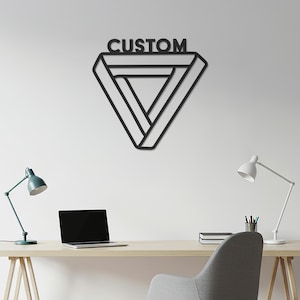 Puede incluir: Arte de pared de metal negro con forma de triángulo geométrico imposible con la palabra "CUSTOM" encima. La obra de arte está montada en una pared blanca. Un escritorio con un portátil y lámparas está en primer plano.