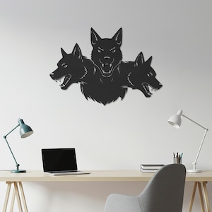 May include: A black metal wall art piece depicting a three-headed wolf, with each head showing sharp teeth. The artwork is mounted on a white wall, creating a striking contrast. The piece is a decorative item.