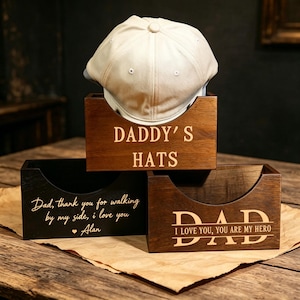 May include: Three wooden boxes with engraved text. The top box, labeled "DADDY'S HATS," holds a white cap. The other boxes have the phrases "Dad, thank you for walking by my side, I love you - Alan" and "DAD I LOVE YOU, YOU ARE MY HERO."
