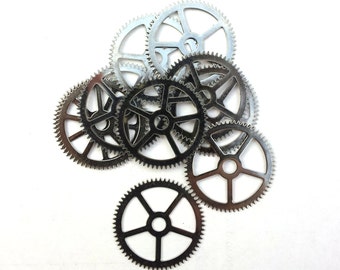 May include: A group of eight silver metal gears of various sizes, arranged in a pile on a white background.