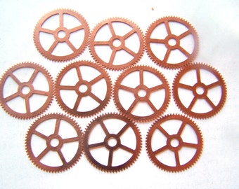 May include: Ten copper-colored metal gears with five spokes each. The gears are arranged in a circular pattern on a white background.