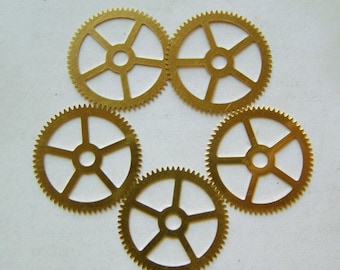 May include: Five gold-coloured metal gears, each with a circular shape and five spokes. The gears are arranged in a circle, with the spokes of each gear pointing towards the centre of the circle.