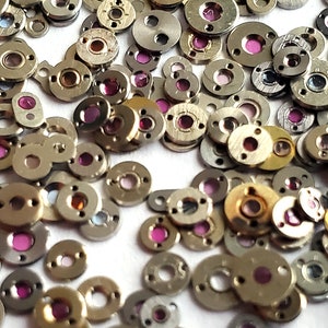 Puede incluir: Una gran colección de pequeñas piezas de reloj redondas de metal en una variedad de colores, incluyendo oro, plata y rosa.