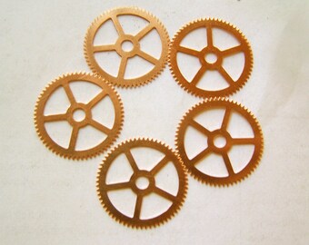 May include: Five small, gold-colored metal gears with five spokes each. The gears are arranged in a circle on a white background.