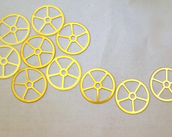 May include: A collection of ten gold-coloured metal gears of varying sizes arranged in a curved line on a light grey background.