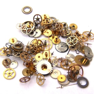 May include: A collection of gold and silver clock gears and cogs, some with intricate designs. The gears are scattered on a white background.