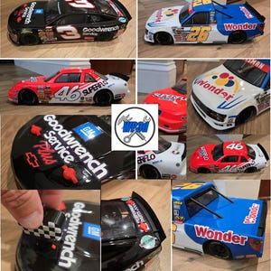 May include: A collection of toy race cars in various colors, including black, red, white, and blue. The cars feature sponsor logos and racing numbers, such as "3", "26", and "46". The cars are detailed with sponsor decals and racing graphics.