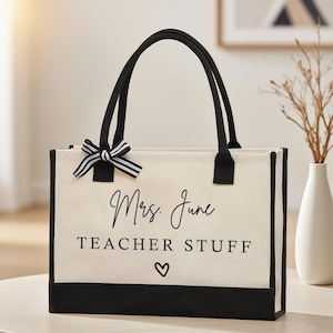 Peut inclure: Sac fourre-tout crème avec garniture, poignées et nœud noirs. Le sac porte l'inscription "Mrs. June TEACHER STUFF" avec un symbole de cœur. Un article décoratif pour les enseignants.