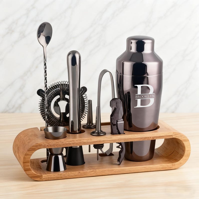 May include: A complete bar tool set in a wooden holder. The set includes a cocktail shaker with the word "Brooklyn" and the letter "D" engraved, a jigger, a strainer, a muddler, a bar spoon, a bottle opener, and other tools.