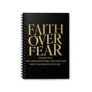 Puede incluir: Cuaderno negro con espiral con letras doradas que dicen "FAITH OVER FEAR" y la escritura Salmos 118.6. El cuaderno también incluye el texto "EL SEÑOR ESTÁ DE MI PARTE; NO TEMERÉ. ¿QUÉ PUEDE HACER EL HOMBRE CONTRA MÍ?"