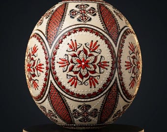 May include: A decorative egg with a cream-colored base, adorned with intricate red and black floral and geometric patterns. The egg features a central floral design and is displayed on a black pedestal. The egg is a unique piece of art.