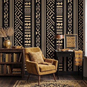 May include: A room featuring wallpaper with a black and tan geometric pattern, a mustard yellow armchair with a matching patterned pillow, a dark wood bookshelf filled with books, and a black desk with a lamp and a framed print.