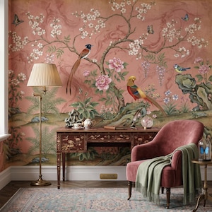 May include: A room featuring a pink floral wallpaper mural with birds, butterflies, and trees. A brass floor lamp with a pleated shade stands next to a dark wood desk with floral inlays. A velvet armchair with a green throw blanket sits nearby.