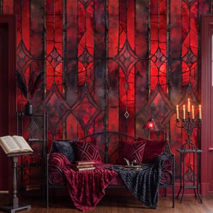 Könnte beinhalten: Eine schwarze Metall-Liege mit roten und schwarzen Samtkissen und einer dunkelgrauen Decke vor einer Wand mit roten Buntglasmustern. Ein schwarzer Metall-Kerzenständer mit fünf brennenden Kerzen steht auf einem passenden Beistelltisch.
