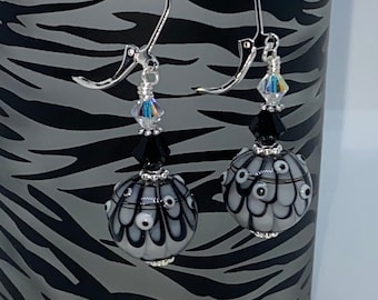 May include: A pair of silver dangle earrings featuring black and white glass beads. The beads have a swirling pattern and are accented with clear crystal beads.
