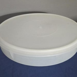 May include: A round, semi-translucent white plastic storage container with a matching flat, circular lid. The container features a smooth, low-profile design with a slightly raised rim on the lid and a simple, functional structure for food storage.