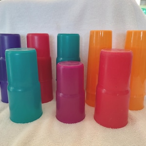 Könnte beinhalten: Eine Sammlung bunter Plastikbecher in verschiedenen Farbtönen, darunter Lila, Rot, Türkis, Magenta und Orange. Die Becher haben ein einzigartiges, abgestuftes Design und sind auf einer weißen Oberfläche angeordnet.