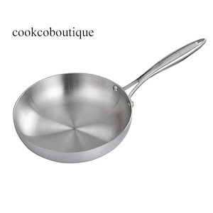 Puede incluir: Una sartén de acero inoxidable con un mango largo. La sartén es redonda con un interior pulido y un mango remachado. El texto "cookcoboutique" está en la esquina superior izquierda.